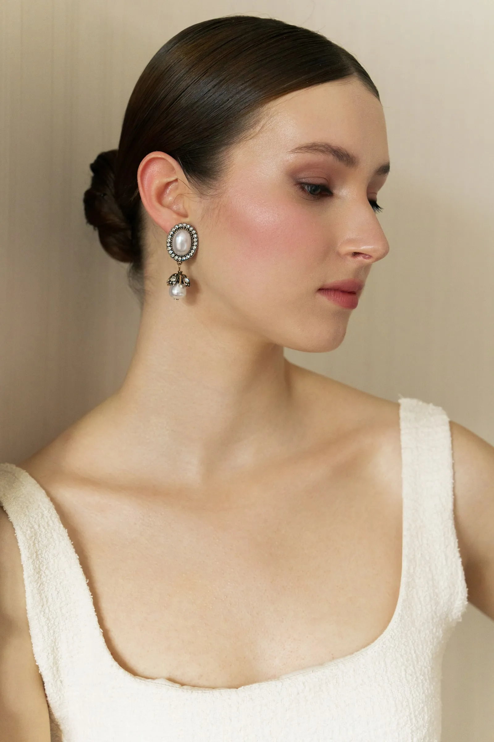 Soft beauty look with a luminous rosy cheek, a clean satin base and a low chignon, worn with pearl drop earrings.
