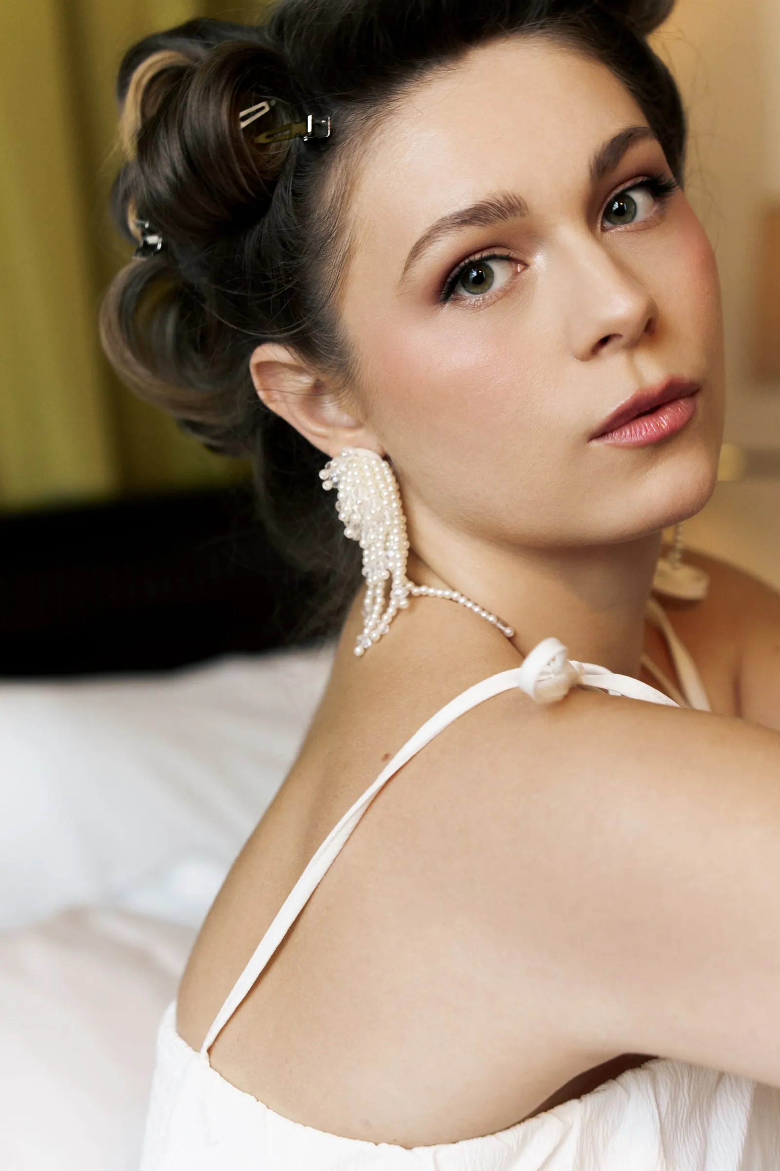 Bridal makeup with a satin skin finish, soft bronze eye and a warm rose lip, worn with a pearl-pinned updo.