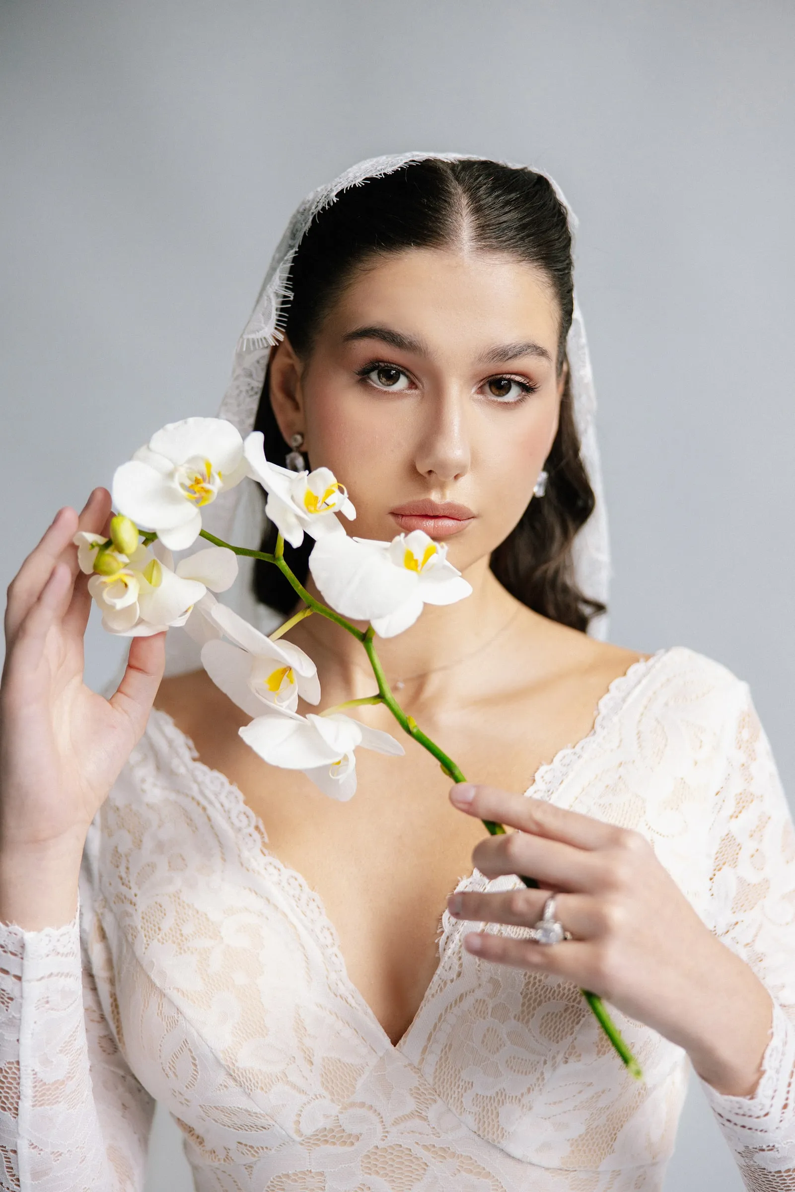 Bridal look with a soft neutral eye, glowing cheeks and a nude lip, worn with lace sleeves and an orchid.