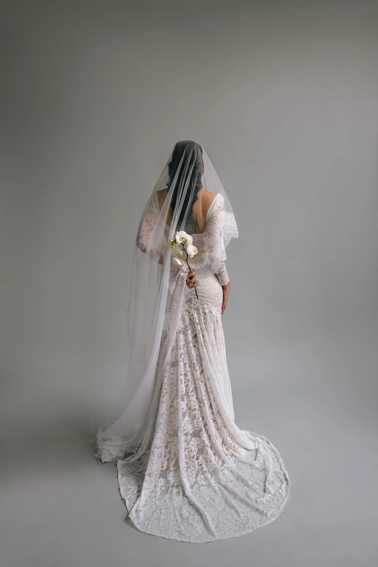 Full-length bridal portrait in a lace gown and veil, makeup kept soft and luminous for daylight.