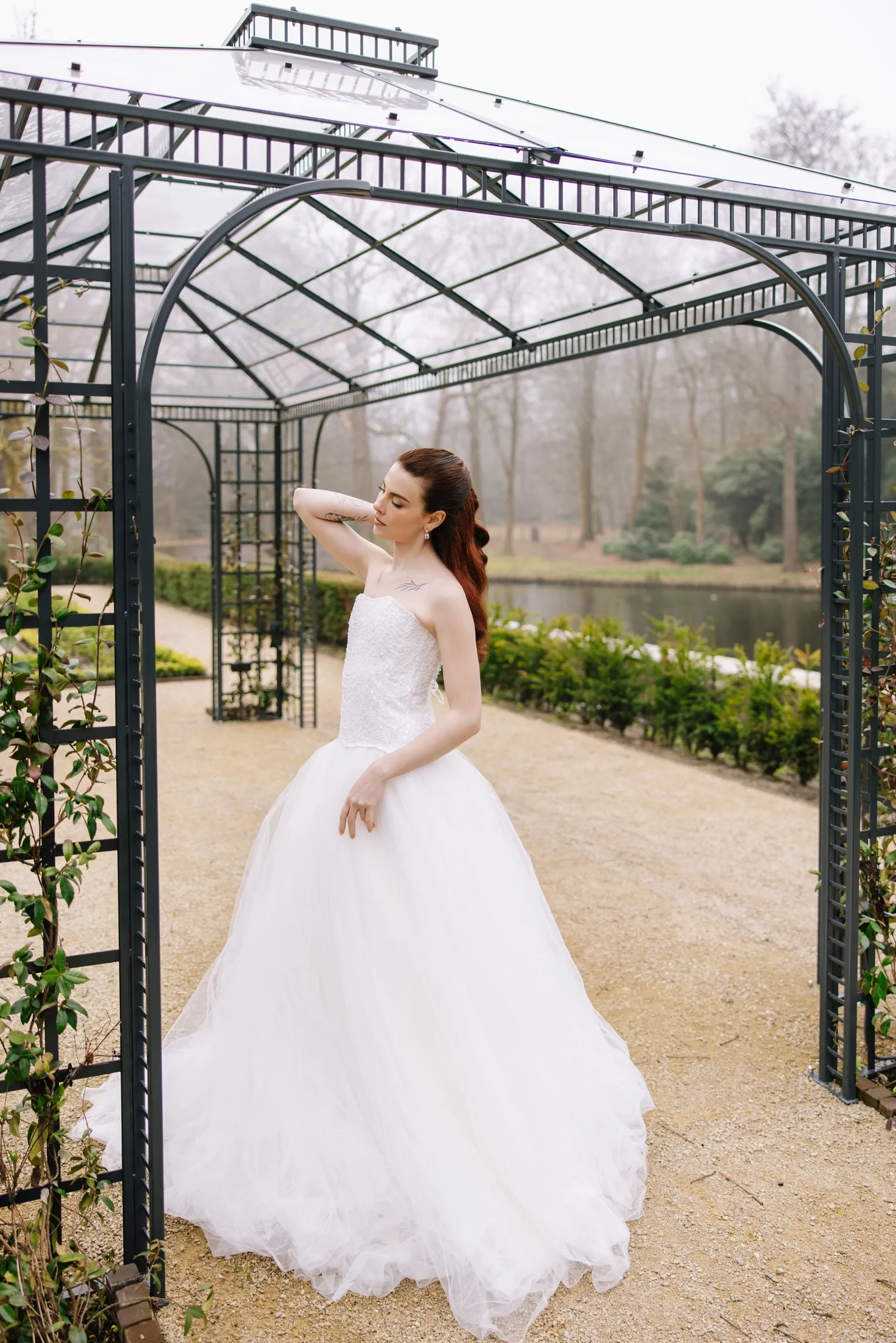 Bride in a tulle ballgown under a garden pergola, with soft daylight makeup and a warm neutral lip.