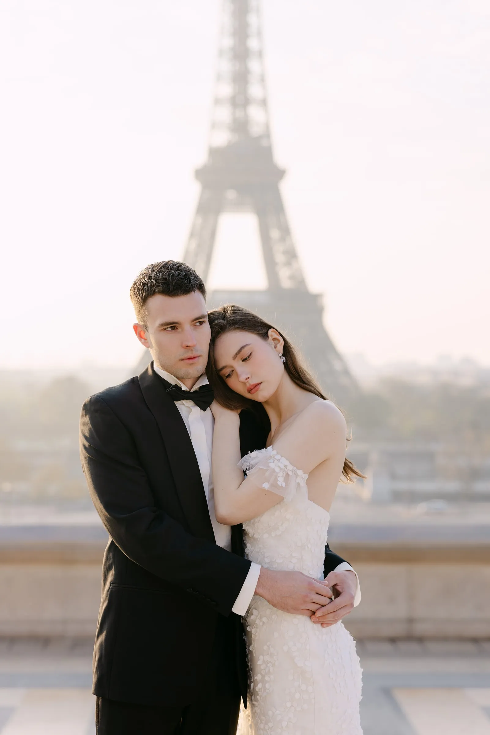 Couple photographed in front of the Eiffel Tower in soft morning haze, with a natural luminous base.