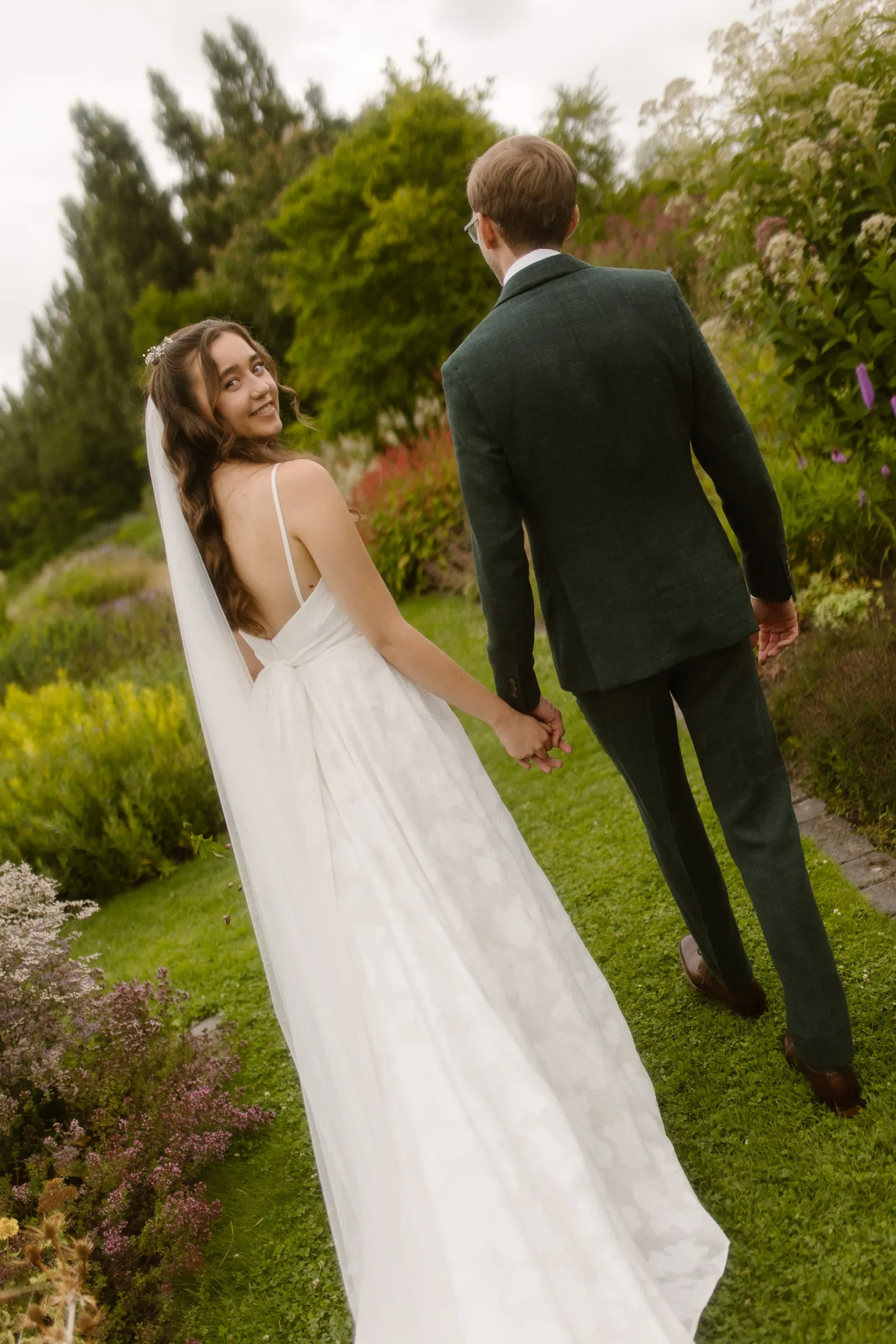 Bride and groom walking through a garden, bridal makeup kept fresh and natural for outdoor daylight.