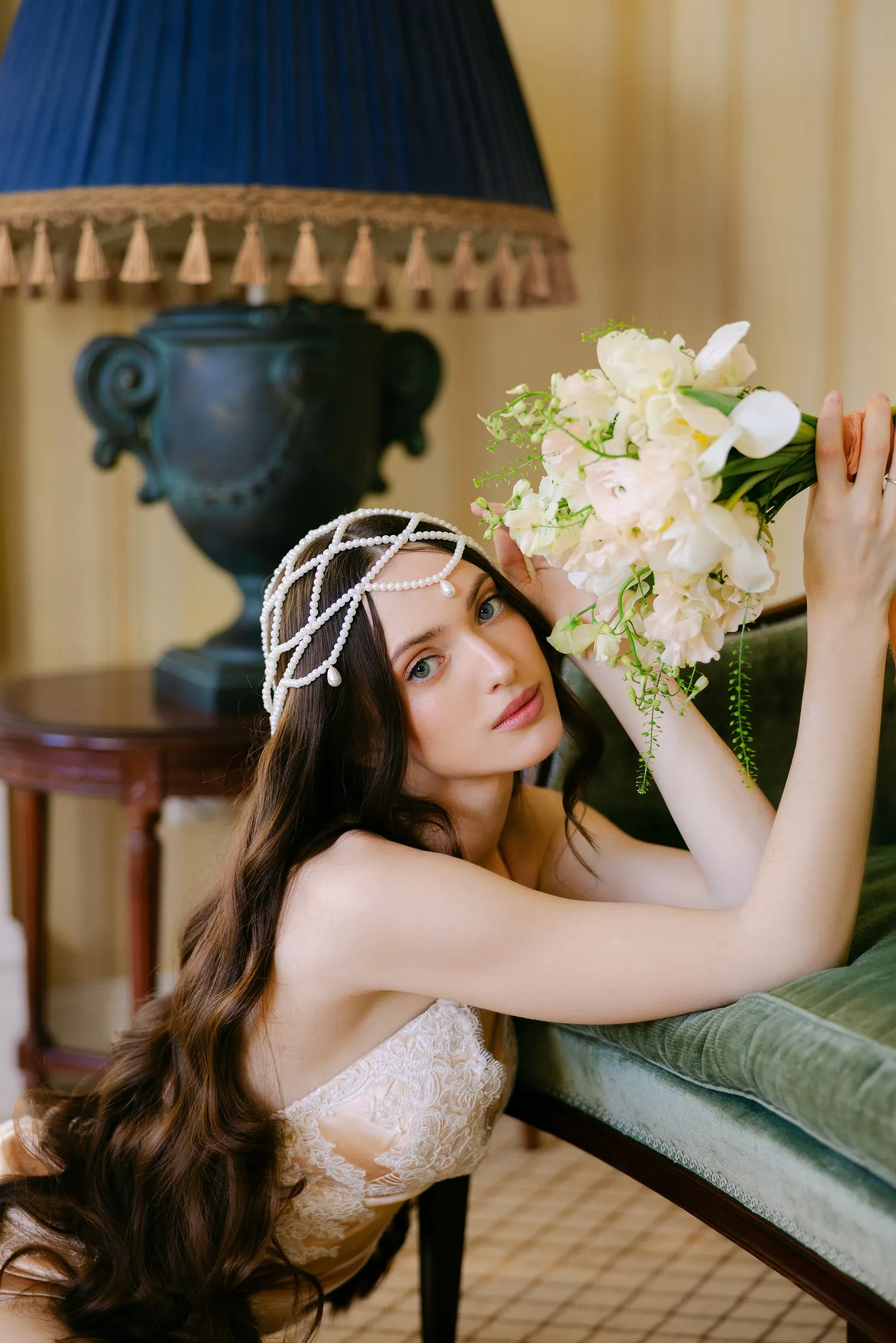 Art-deco inspired look with a beaded headpiece, defined eye and long waves against a green velvet sofa.