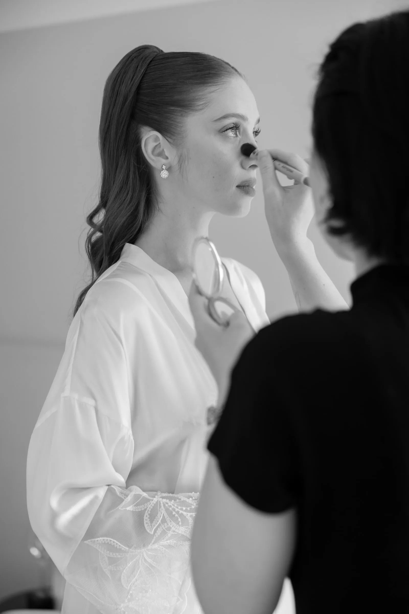 Black and white behind-the-scenes frame of makeup being applied to a bride during morning preparations.